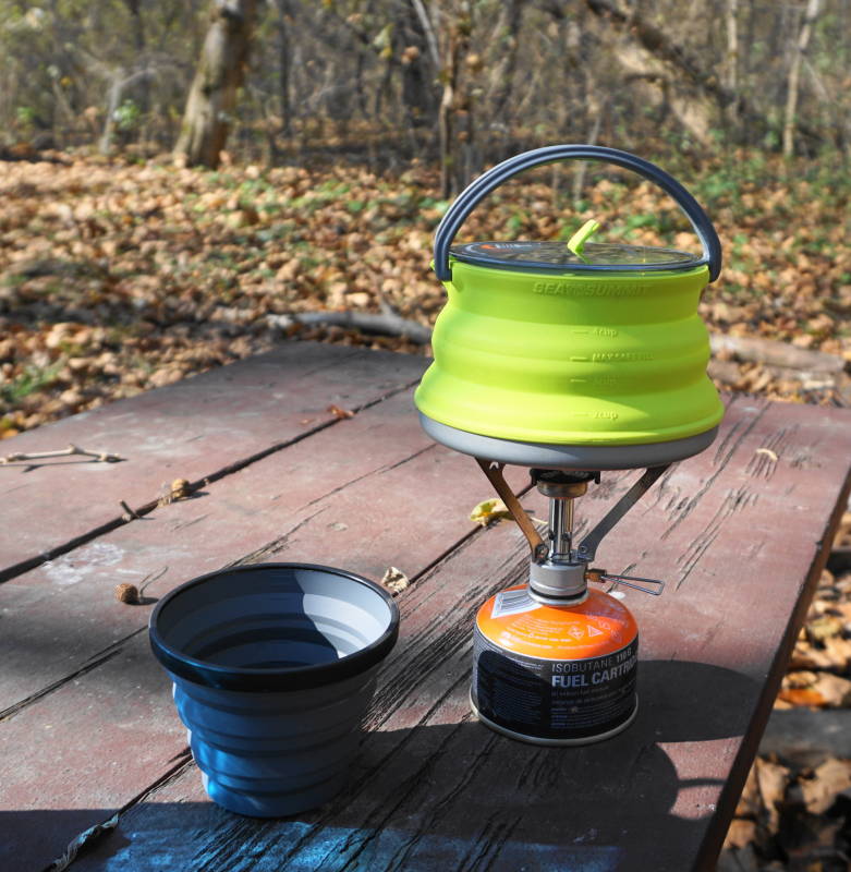 Lightweight camping stove with a SeaToSummit X-pot Kettle and X-cup on a picnic table.