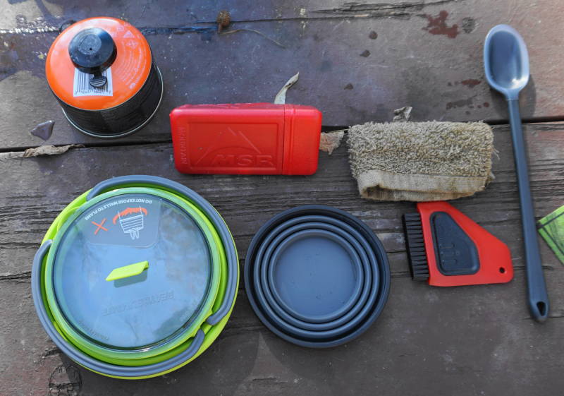 Photo of collapsed pot and cup with other accessories including stove and cleaning supplies.